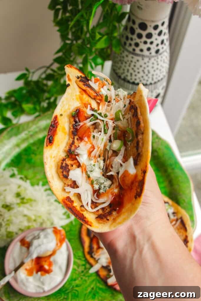 Holding a buffalo chicken taco with more in the background.