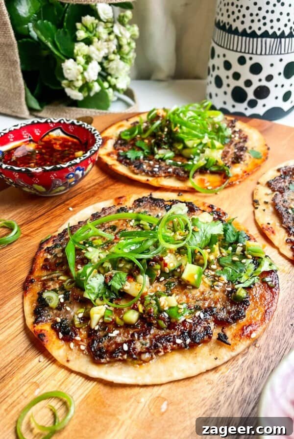 Three dumpling tacos on a wooden board with chilli oil on the side.