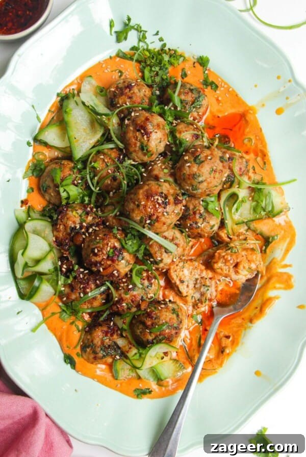 Dumpling meatballs on gochujang sauce with pickled cucumber on an oval platter.