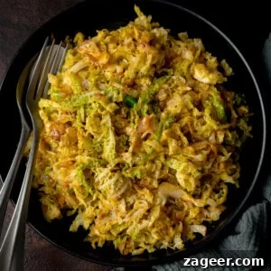 Pan Sautéed Cabbage with Garlic and Crispy Edges 6 Overhead image of a black bowl filled with sauteed cabbage with a fork and spoon on the side.