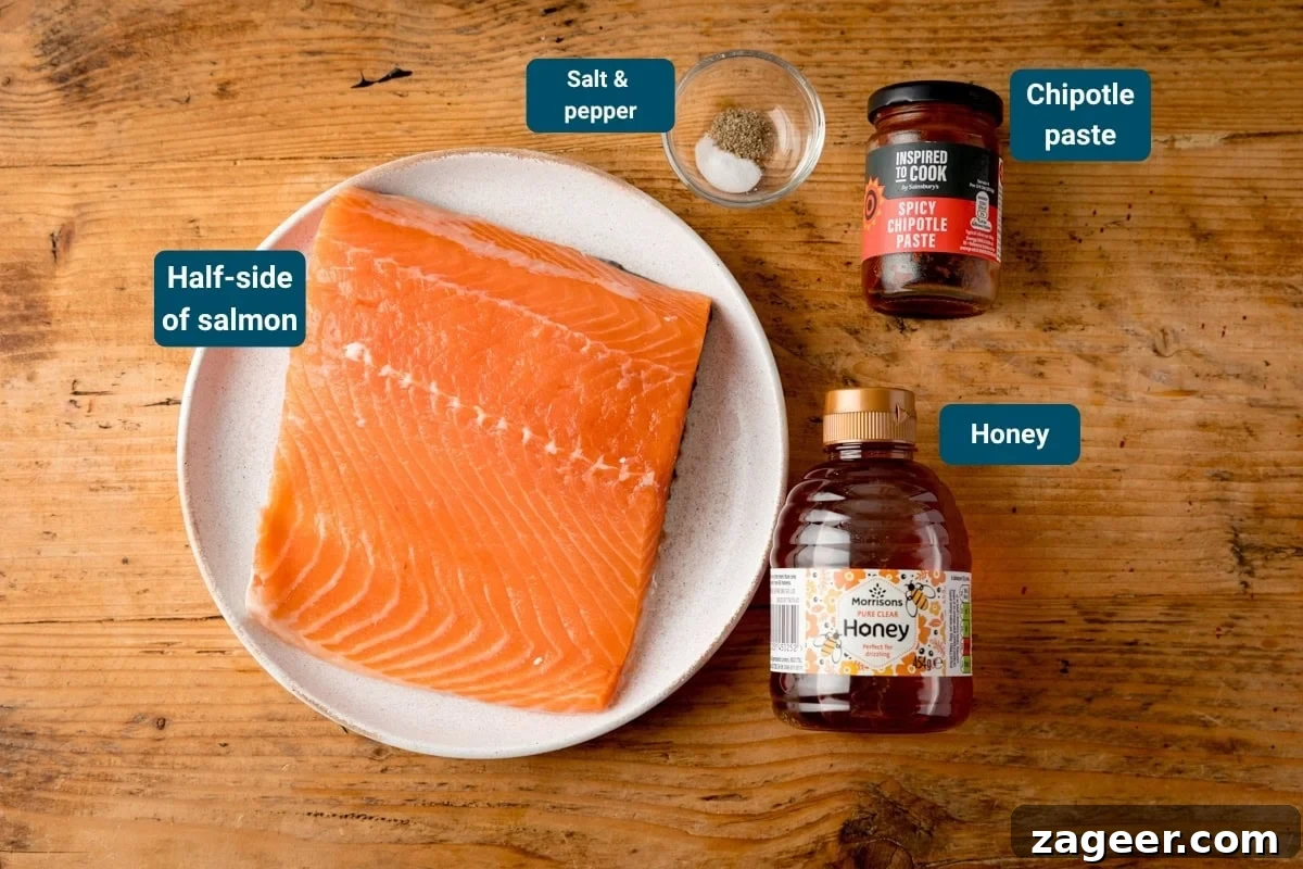 A half-side of raw salmon on a plate, with small bowls of salt and pepper, a jar of chipotle paste, and a bottle of honey on a wooden surface.