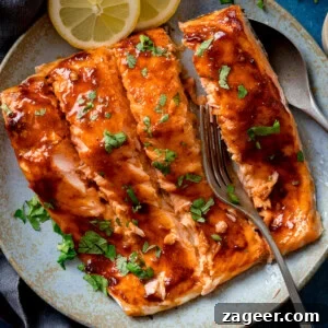 Glazed salmon fillets garnished with chopped herbs on a light blue plate, with lemon slices and a fork at the side.