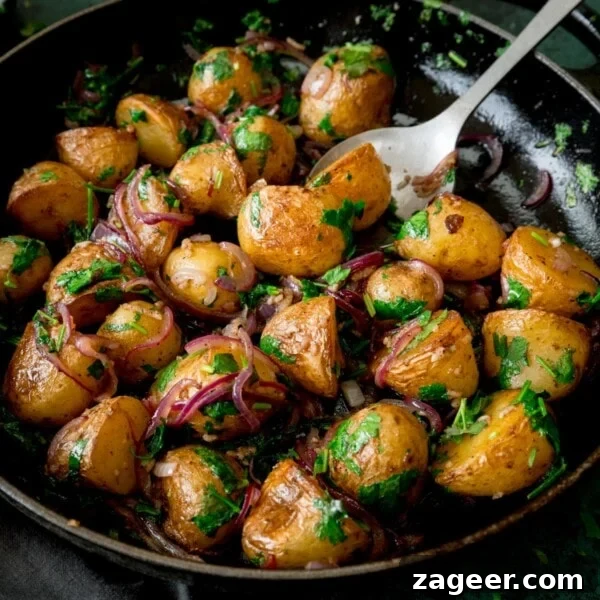 Pan-fried potatoes with garlic, coriander and red onion in a black pan.
