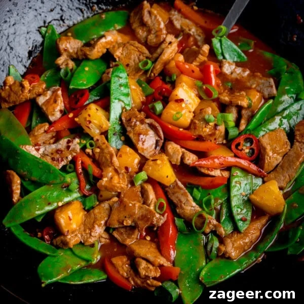 Pineapple pork stir-fry in a wok with pork, peppers and pineapple.