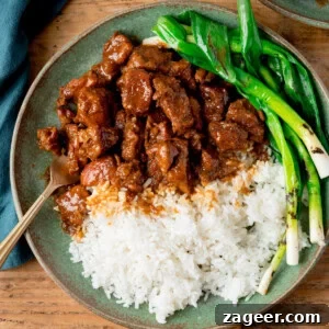A green plate with white rice, Vietnamese-style caramel pork and grilled spring onions (scallions), with a fork on the side. The plate is on a wooden surface.