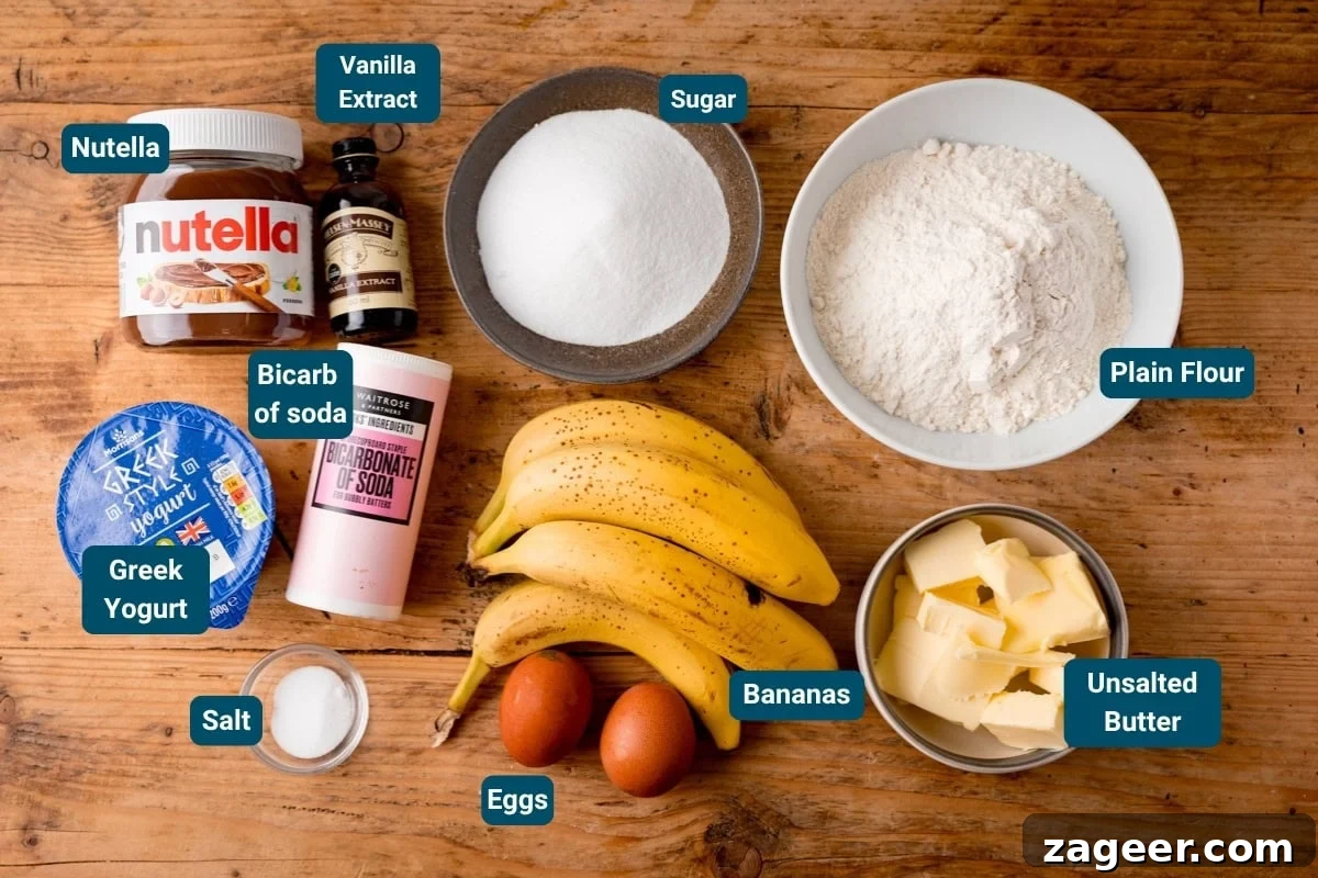 Ingredients on a wooden surface for Nutella Banana Bread including Nutella, vanilla extract, sugar, plain flour, butter, bananas, eggs, Greek yoghurt, bicarbonate of soda, and salt—all ingredients are labelled.