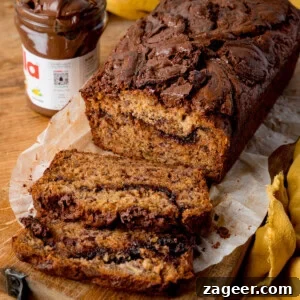 A loaf of Nutella Banana Bread with rich chocolate swirl is sliced on baking parchment, with a jar of Nutella in the background on a rustic wooden surface.
