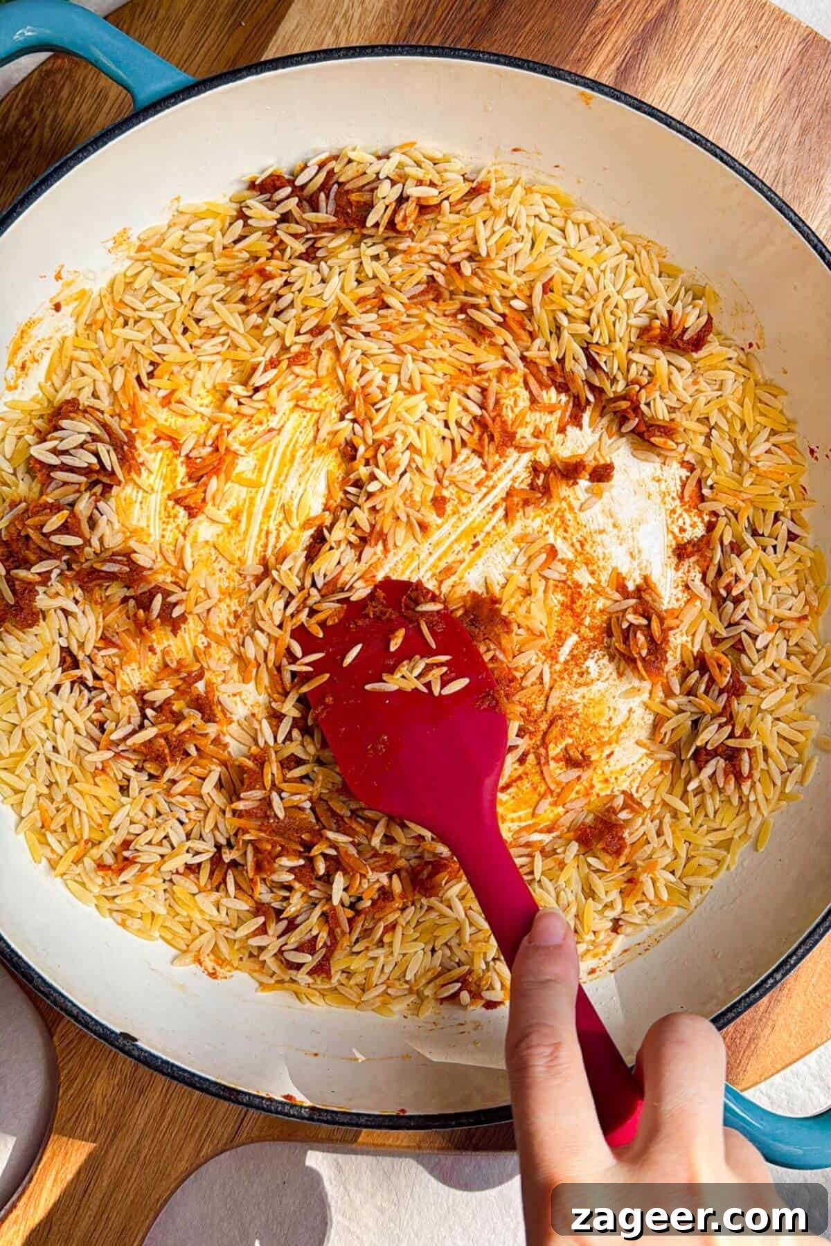 One-Pot Thai Red Curry Chicken Orzo for Weeknight Dinners 7 Orzo being mixed through red curry paste in a pan.