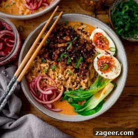 A bowl of spicy pork coconut curry ramen with sliced boiled eggs, pak choi, pickled onions and spring onions.