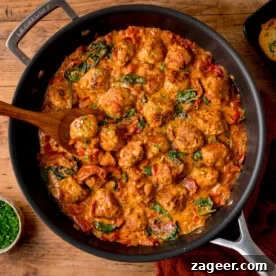 A frying pan filled with Tuscan Chicken Meatballs in creamy tomato sauce with spinach and herbs.