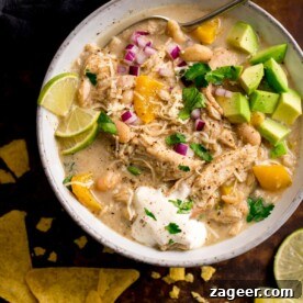 white chilli chicken con carne in a white bowl topped with lime wedges, avocado chunks and red onion. Tortilla crisps next to the bowl.