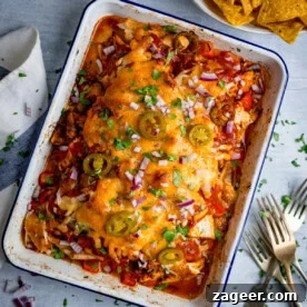 A baked casserole dish filled with tender baked salsa chicken, topped with melted cheese, jalapeños, red onions, and chopped herbs; tortilla crisps sit in a bowl nearby.