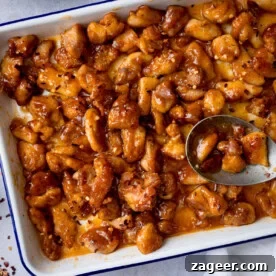 A square, overhead shot of Baked Honey Garlic Chicken in a white tray with a dark blue rim, with a spoon and scattered chilli flakes.