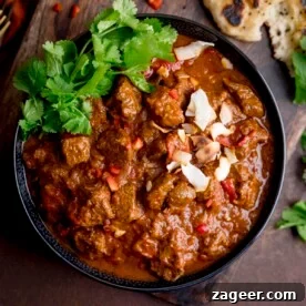 Square image of beef curry topped with coriander, chillies and toasted coconut in a black bowl.